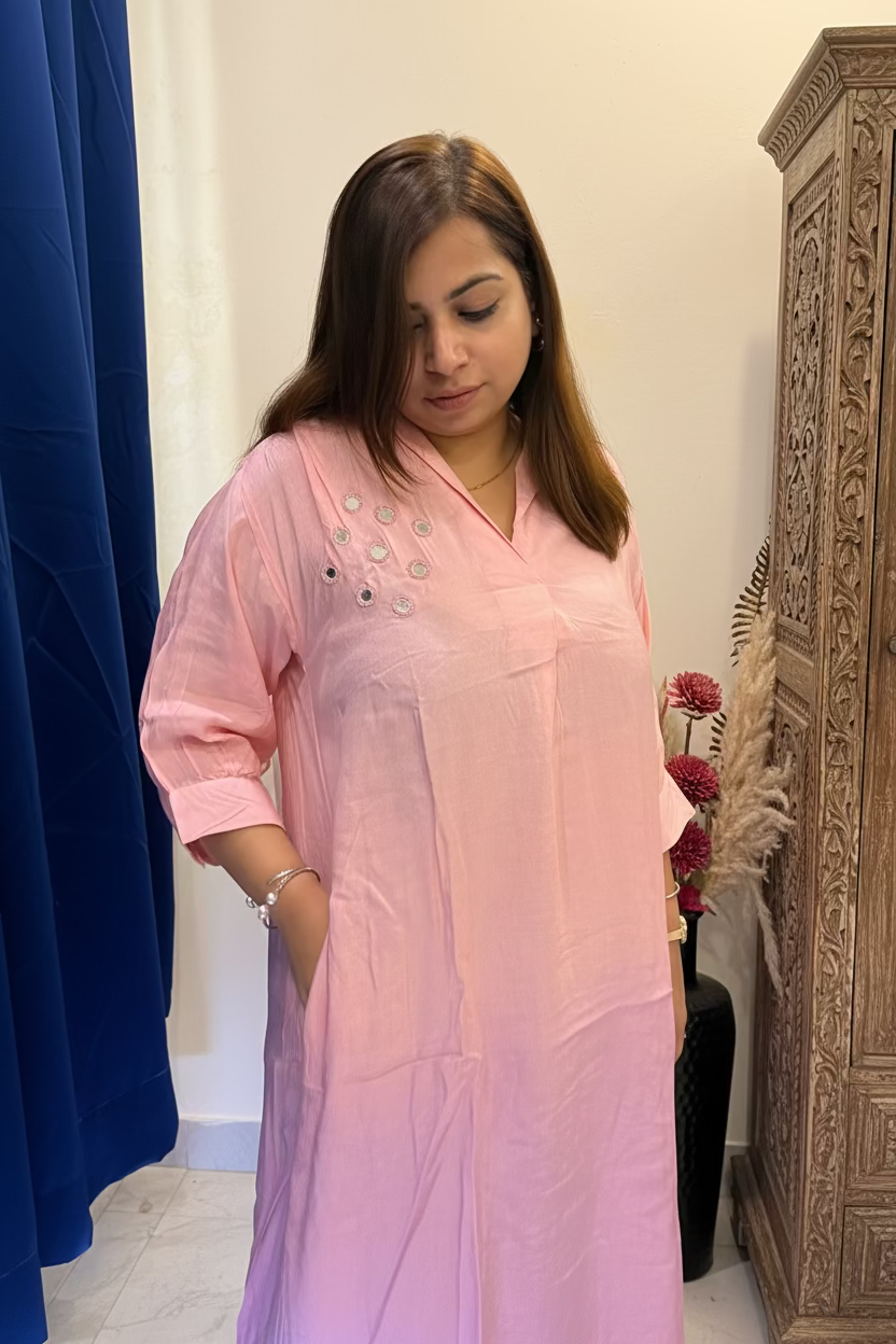 A woman wearing a light pink cotton kurta with silver mirror work embellishments on the chest, standing in an indoor setting.