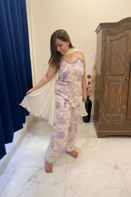 A woman modeling a light purple and white floral print salwar suit set with a white dupatta in a bedroom setting.