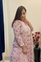 A woman wearing a pink and white floral print kurta with lace trim, standing in front of a mirror in an indoor setting.