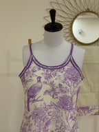 A sleeveless camisole tank top displayed on a dress form mannequin. The top features a purple and cream toile-style print with a bird and floral motifs, and a purple braided trim along the neckline.