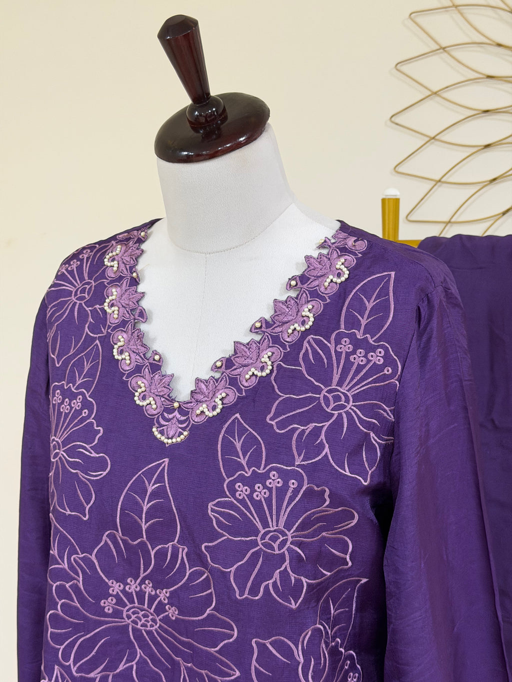 A purple long-sleeve tunic top with white floral embroidery and a scalloped embroidered neckline, displayed on a white mannequin torso.