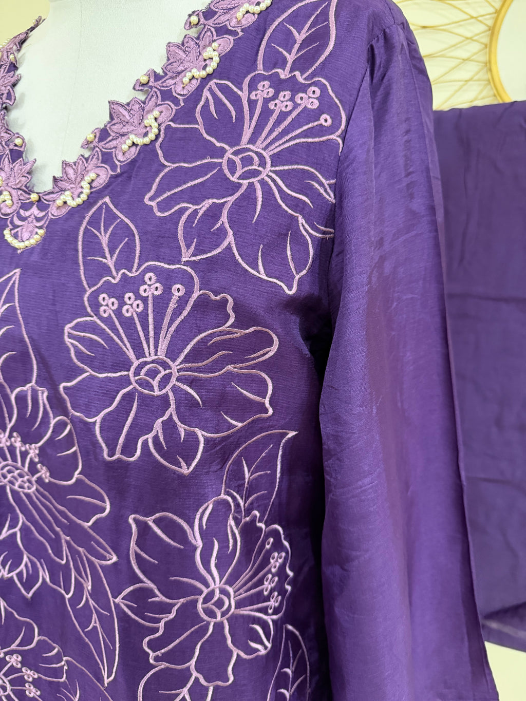 A close-up of a purple garment with white floral embroidery.