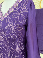 A close-up of a purple garment with white floral embroidery.