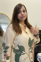 A woman with long brown hair wearing a cream-colored long-sleeve kurta with a green leaf and peach floral print, standing in front of a mirror in an indoor setting.