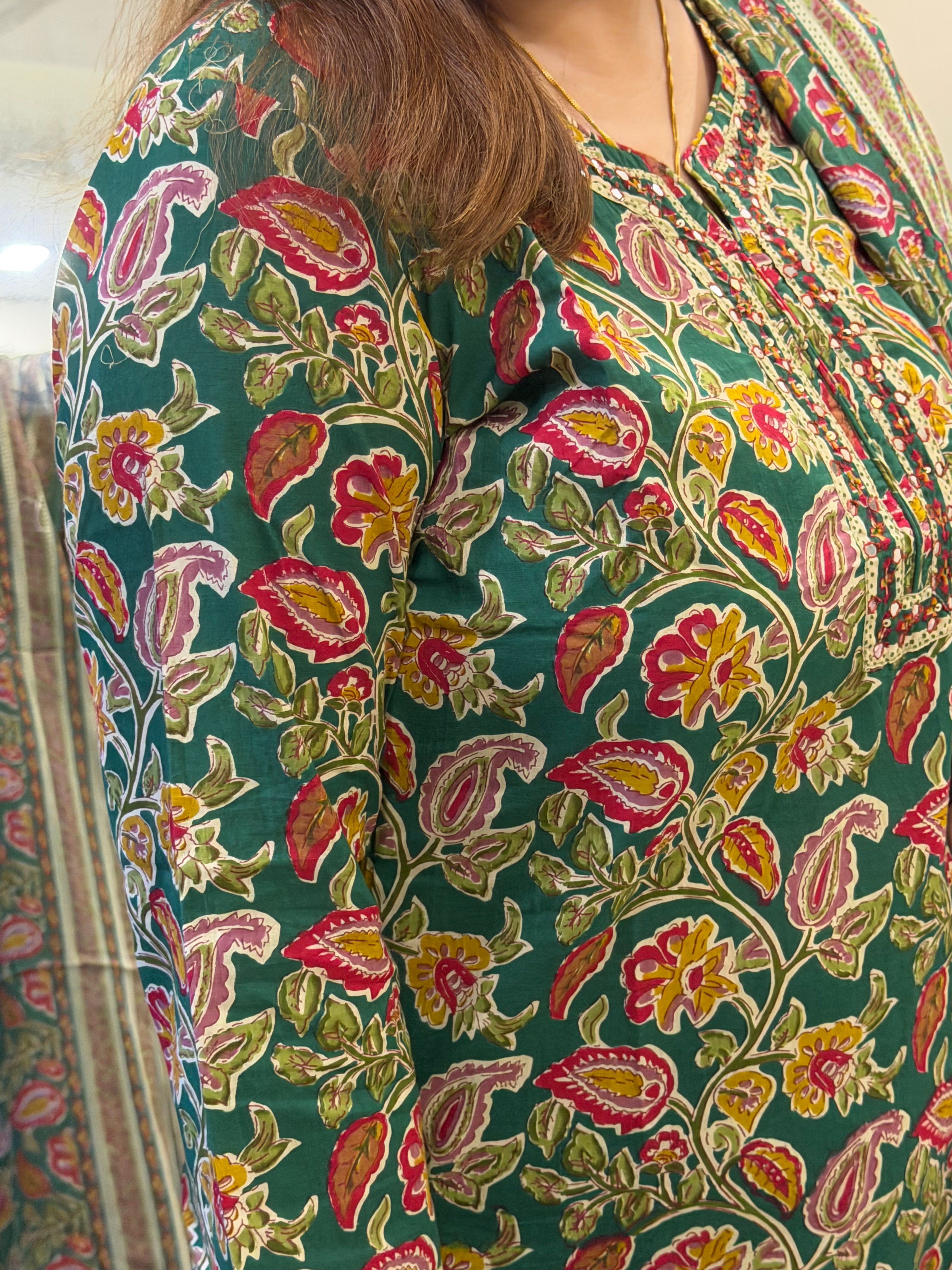 A close-up of a person wearing a green kurta with a colorful floral and paisley block print in pink, yellow, and beige, featuring a V-neckline with embroidered detailing.