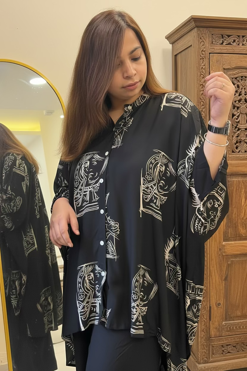 A woman wearing a black button-up shirt with a white graphic print of stylized faces, standing in front of a mirror in an indoor setting.
