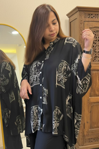 A woman wearing a black button-up shirt with a white graphic print of stylized faces, standing in front of a mirror in an indoor setting.