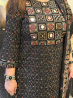 A close-up of a woman wearing a black three-piece salwar kameez suit set with a printed pattern, featuring a printed kameez shirt with mirror work, matching trousers, and a dupatta.